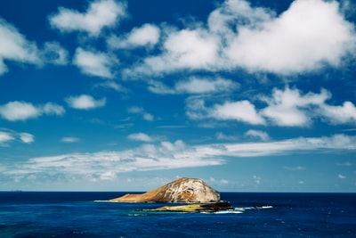The blue sky white clouds during the day the sea surface brown rock formation
